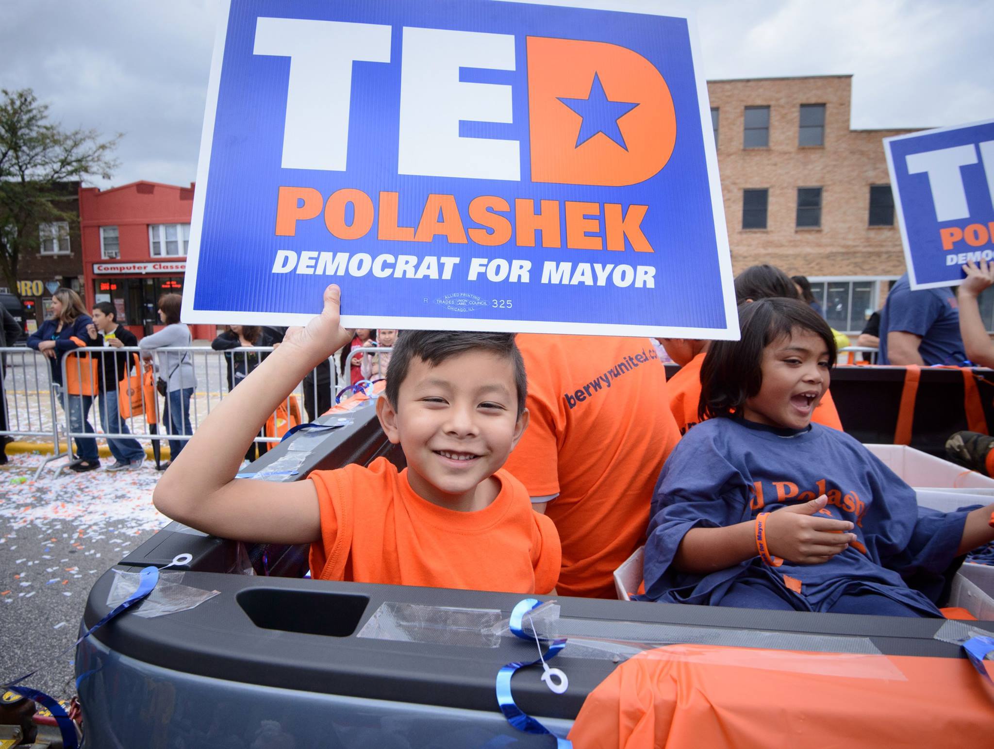 Boy riding in convertible holding campaign sign with campaign logo.